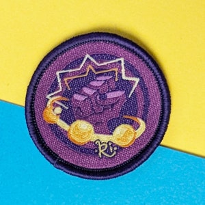 以下が含まれることがあります： 紫と白のデザインの刺繍パッチ。メガネと星型の頭を持つ漫画のキャラクターが特徴です。パッチは濃い紫色の縁取りで、「R」と「Eldritch Rach」の文字が入っています。