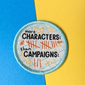 May include: A blue and white embroidered patch with the text "more CHARACTERS: than CAMPAIGNS:" and tally marks.