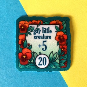 Op de afbeelding: Een vierkante sticker in turquoise blauw met een witte rand en een bloemige rand. De sticker zegt "gay little creature +5 20".