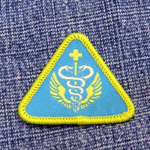 May include: A blue and yellow triangular patch with a white medical symbol and wings. The symbol is a caduceus, a staff with two snakes intertwined around it, topped with a cross.
