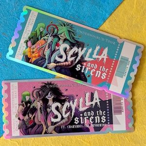 May include: Two concert tickets with a holographic finish. The tickets feature the text "SCYLLA and the sirens" with illustrations of characters. The top ticket is teal and the bottom ticket is pink. The tickets are on a blue and yellow background.