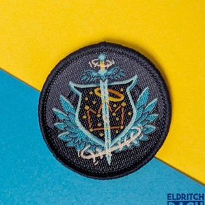 May include: A black circular patch with a blue and gold embroidered design. The design features a sword, a crown, and wings. The text "Eldritch Rach" is visible in the lower right corner of the image.