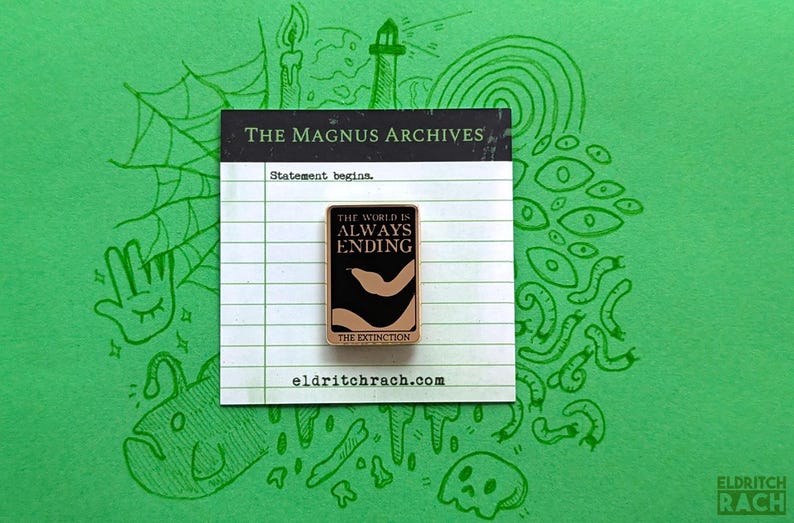 Pu&ograve; includere: Spilla rettangolare con la scritta "THE WORLD IS ALWAYS ENDING" su sfondo nero con un disegno beige. La spilla &egrave; su una carta bianca con la scritta "THE MAGNUS ARCHIVES" e "Statement begins." Lo sfondo &egrave; verde con scarabocchi verdi.