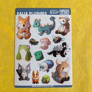 May include: A sticker sheet featuring various cartoon plushie designs, including a fox, dragon, deer, and frog. The sheet has the text "PALIA PLUSHIES" and "ATOMIC ELDRITCH BUN+RACH" at the top, and the website address www.eldritchrach.com at the bottom.