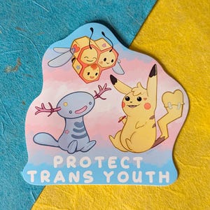 Pode incluir: Um autocolante com personagens de desenhos animados, incluindo um Pikachu amarelo, uma criatura azul semelhante a um axolotl e uma colmeia com abelhas sorridentes. O autocolante tem o texto "PROTECT TRANS YOUTH" em letras azuis. O fundo é uma mistura de azul e amarelo.