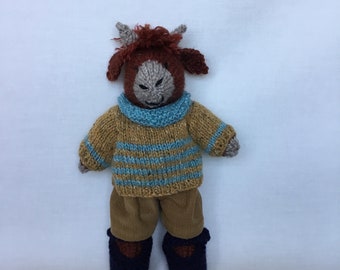 Handmade rust colour knitted highland cow, light turquoise/ mustard fleck jumper, mustard cord trouser’s and dark brown shoes.