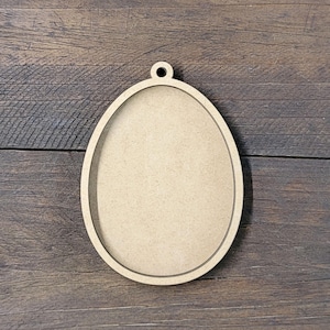 May include: A wooden oval-shaped ornament with a hole at the top for hanging. The ornament is unfinished and ready to be painted or decorated.