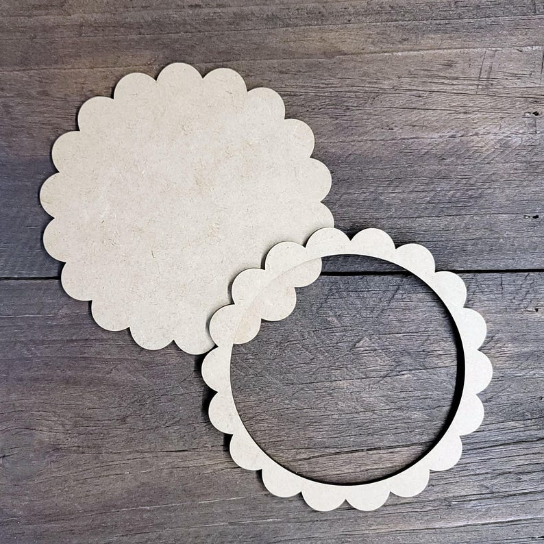 May include: Two unfinished wooden craft pieces with a scalloped edge. One is a solid circle, and the other is a ring with the same scalloped design. The pieces are light brown and sit on a dark wood grain surface.