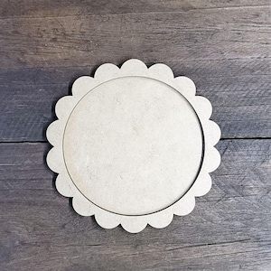 May include: A round, unfinished wooden craft blank with a scalloped edge. The blank has a circular interior and is made of light-colored wood, perfect for painting or other DIY projects.