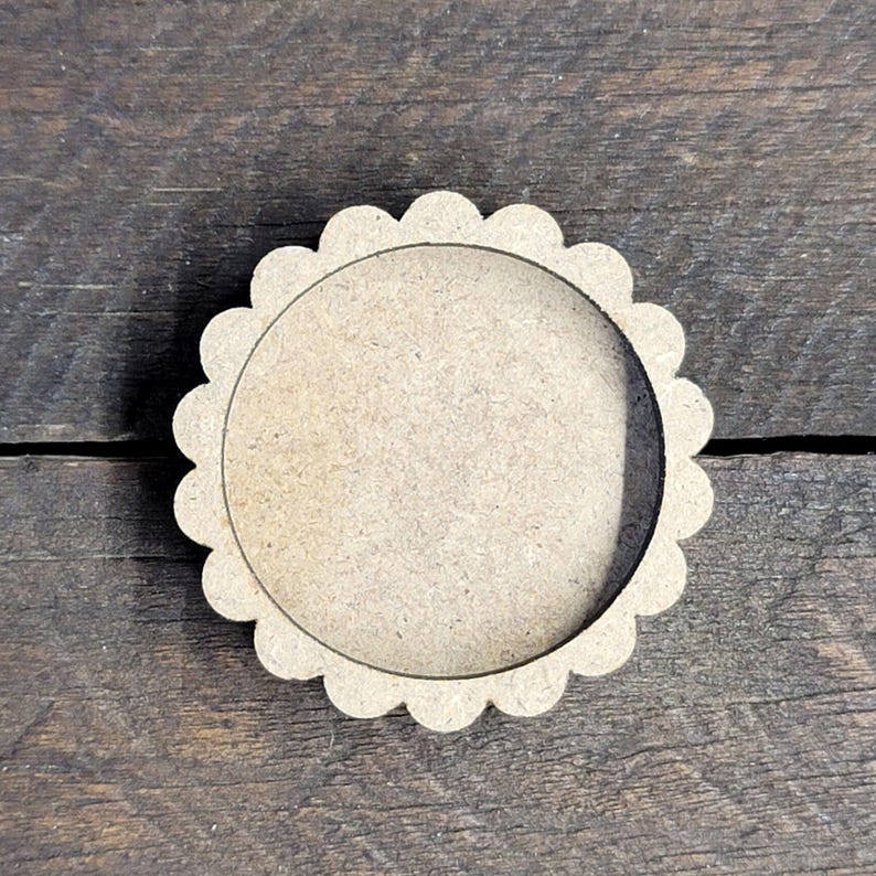 May include: A round, unfinished wooden craft blank with a scalloped edge. The blank has a circular cutout in the center and is made of light brown wood. The design is simple and suitable for various DIY projects.