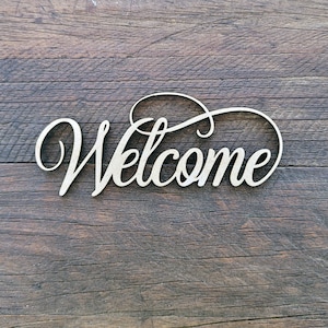 May include: A wooden sign with the word "Welcome" in a cursive font. The sign is on a dark brown wooden background.