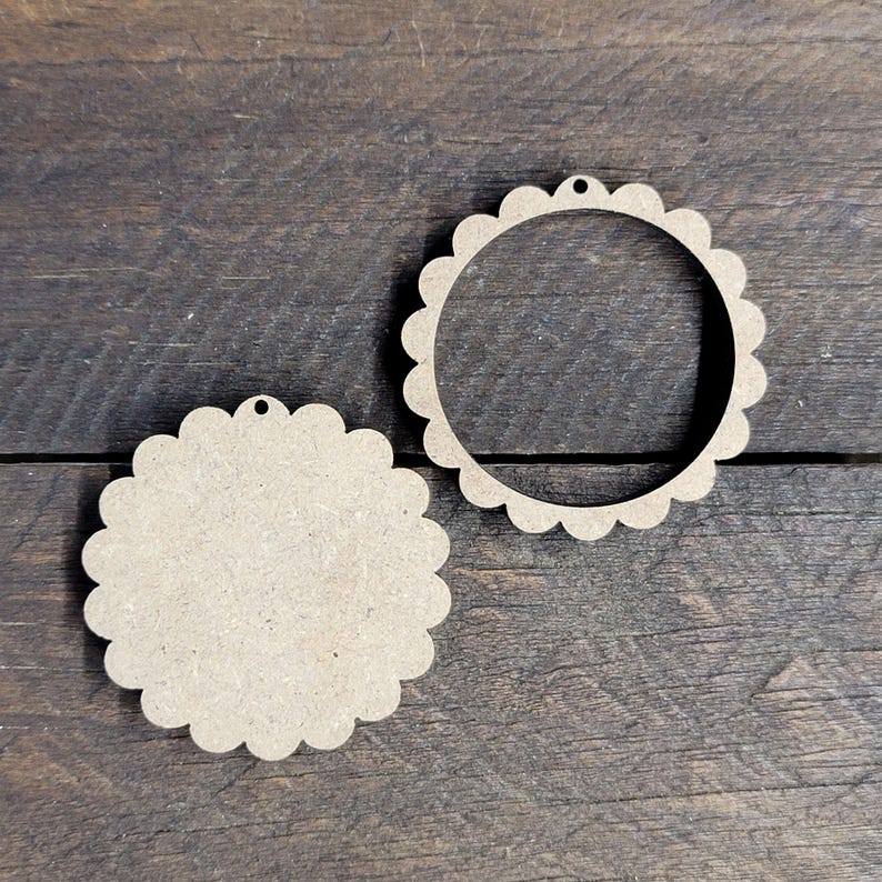 May include: Two unfinished wooden ornaments with scalloped edges. One is a solid circle, and the other is a ring. Each has a small hole at the top for hanging. The ornaments are made of light brown wood.