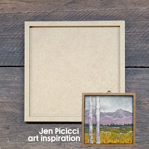 May include: A square light-colored wooden frame with a blank center and a smaller square framed artwork featuring two white birch trees in the foreground, purple mountains in the distance, and a yellow field, with the text Jen Picicci art inspiration.