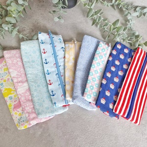 Può includere: Un set di nove astucci per matite in tessuto con diversi motivi. I motivi includono ancore, cupcake, fiori e strisce. Gli astucci sono tutti in tonalità di blu, rosa e rosso.