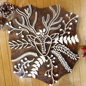 May include: A wooden block with a deer design carved into it. The deer has large antlers and is surrounded by floral elements. The block is brown with white accents. Two pinecones and a red star-shaped ornament are also present.