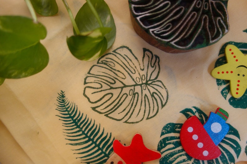 May include: A close-up of a light brown surface with various green leaf designs and a yellow starfish with red dots. There is also a red and blue boat with white dots and a red starfish.
