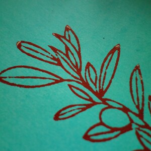 Puede incluir: Una superficie de papel turquesa vibrante con una impresi&oacute;n de tinta roja oscura de una rama bot&aacute;nica. La ilustraci&oacute;n muestra un tallo central con m&uacute;ltiples hojas alargadas y un peque&ntilde;o fruto redondo, representado en un estilo de l&iacute;nea audaz y texturizado.