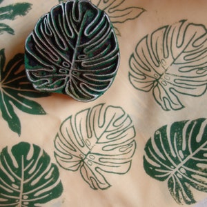 May include: A close-up of a green leaf-shaped rubber stamp on a beige surface. The stamp is surrounded by several green leaf prints.