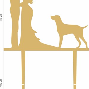 May include: A wedding cake topper featuring a couple kissing, with a dog standing behind them. The topper is made of wood and is painted gold. The couple is 14 cm tall and the dog is 9 cm tall.