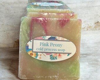 May include: Stacked bars of Pink Peony cold process soap. The soap has layers of pink, green, and yellow hues. Each bar is wrapped in clear plastic with an oval label that reads "Pink Peony cold process soap."