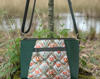 May include: A crossbody bag featuring a central panel with a repeating geometric pattern of orange and pink tulips on a light background, flanked by solid dark green side panels, a dark green adjustable strap, and a horizontal zippered front pocket.