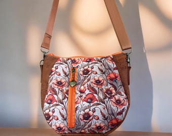 May include: A crossbody bag featuring a floral pattern with red and orange poppies on a light background. The bag has brown cork side panels, an orange vertical zipper with a heart-shaped charm, and a matching brown adjustable shoulder strap.