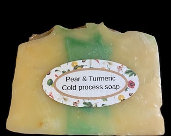 May include: A bar of cold process soap with a pear and turmeric scent. The soap has a light yellow base with a green stripe and a floral label that reads "Pear & Turmeric Cold process soap".