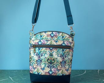 May include: A crossbody bag featuring a damask-inspired pattern with blue butterflies, teal accents, and a solid dark blue base. The bag includes a horizontal zippered front pocket, a top zipper closure, and an adjustable dark blue fabric shoulder strap.
