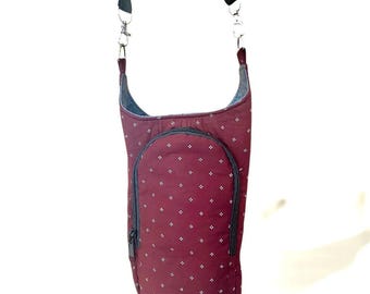 May include: A burgundy crossbody bag with a repeating white diamond pattern. The bag has a black zipper, a black adjustable strap, and silver-colored metal clasps. The bag is designed to be worn over the shoulder.
