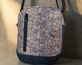 May include: A crossbody bag featuring a brown and black snakeskin pattern on the main body, a solid black base, and a vertical black zippered pocket on the front. The bag includes a black adjustable shoulder strap attached to the top sides.