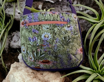 May include: A purple and green floral print crossbody bag with a zippered pocket and a purple strap.