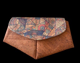 May include: A brown cork clutch with a flap featuring a colorful, patterned design. The clutch has a geometric shape and a textured surface. The flap has a variety of colors including blue, orange, and pink.