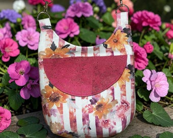 May include: A floral crossbody bag with a red cork pocket. The bag features a white and red striped pattern with watercolor-style flowers in shades of orange, yellow, and purple. The strap and top of the bag have a matching floral design.