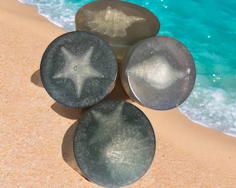May include: Four round soaps with a shimmery, translucent finish. Each soap features a different design of a starfish.