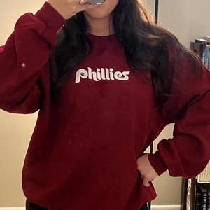 Puede incluir: Una sudadera color granate con un logotipo blanco de "Phillies" en una fuente retro.
