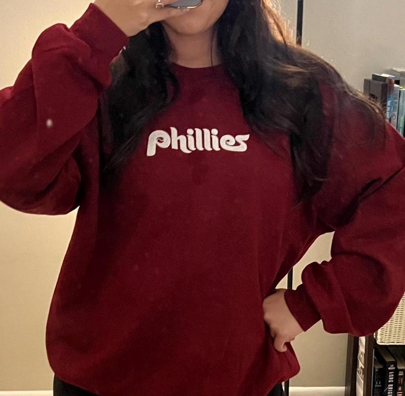 Puede incluir: Una sudadera color granate con un logotipo blanco de "Phillies" en una fuente retro.