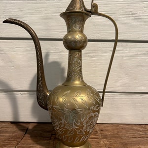 May include: A brass teapot with a floral design. The teapot has a long spout and a handle that is attached to the lid. The lid has a finial on top.