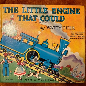 May include: A vintage children's book cover featuring a blue train engine with a smiling face, pulling a train car up a hill. The book title is "The Little Engine That Could" by Watty Piper. The cover is illustrated in a cartoon style with a yellow background.
