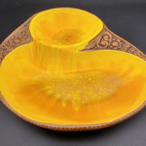 May include: A vintage, two-section serving dish with a bright yellow interior and a brown, textured rim. The dish has a small, round bowl and a larger, oval-shaped section. The rim features a decorative floral pattern.