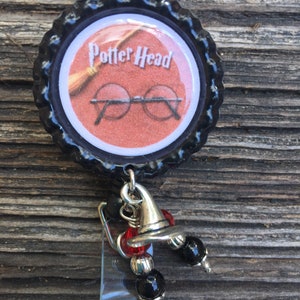 May include: A black bottle cap badge reel with the words "Potter Head" and an image of glasses and a broom. The badge reel has a silver charm of a wizard hat and black and red beads.