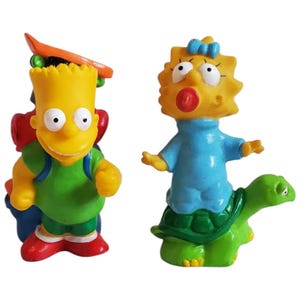 May include: Two yellow Simpsons character figurines. Bart Simpson is wearing a green shirt and carrying a blue backpack with a skateboard on his back. Lisa Simpson is wearing a blue dress and riding a green turtle.