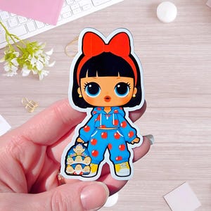 May include: A die-cut sticker featuring a cartoon character with black hair, a large red bow, and big blue eyes. The character wears a blue hoodie and matching sweatpants with a red apple pattern, yellow sneakers, and carries a small backpack.