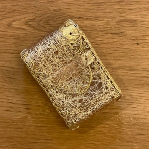 May include: A small, rectangular, gold-colored clutch with a delicate, lacy overlay. The clutch features a flap closure and is made with intricate wire detailing. The overall design is ornate and elegant, suggesting a vintage or handcrafted style.