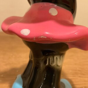 Op de afbeelding: Een zwart keramiek beeldje van een vrouw die een roze rok met witte stippen draagt. De rok is gerimpeld en de vrouw staat op een blauwe basis.