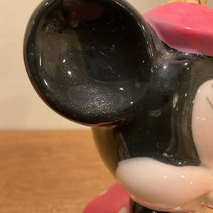 Op de afbeelding: Een zwart-witte keramische figuur van Mickey Mouse met een roze hoed. De figuur zit en heeft een gedetailleerd gezicht.