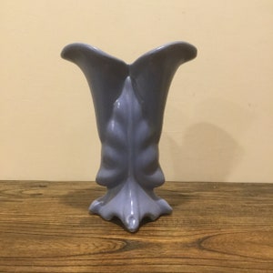 May include: A light blue ceramic vase with a leaf design. The vase has a wide opening and a narrow base.