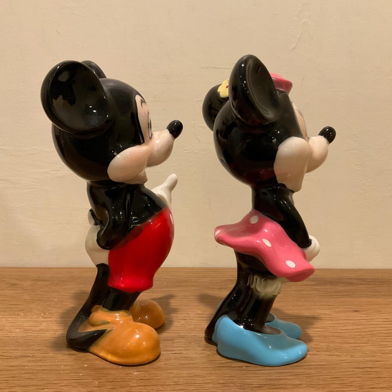 Op de afbeelding: Een paar keramische beeldjes van Mickey Mouse en Minnie Mouse. Mickey draagt een rode broek en gele schoenen. Minnie draagt een roze gebloemde jurk en blauwe schoenen.