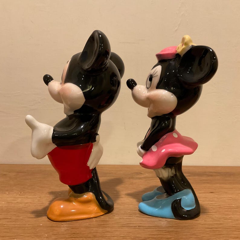 Op de afbeelding: Een paar keramische Mickey Mouse en Minnie Mouse beeldjes. Mickey draagt een rode broek en gele schoenen. Minnie draagt een roze jurk met witte stippen en blauwe schoenen.