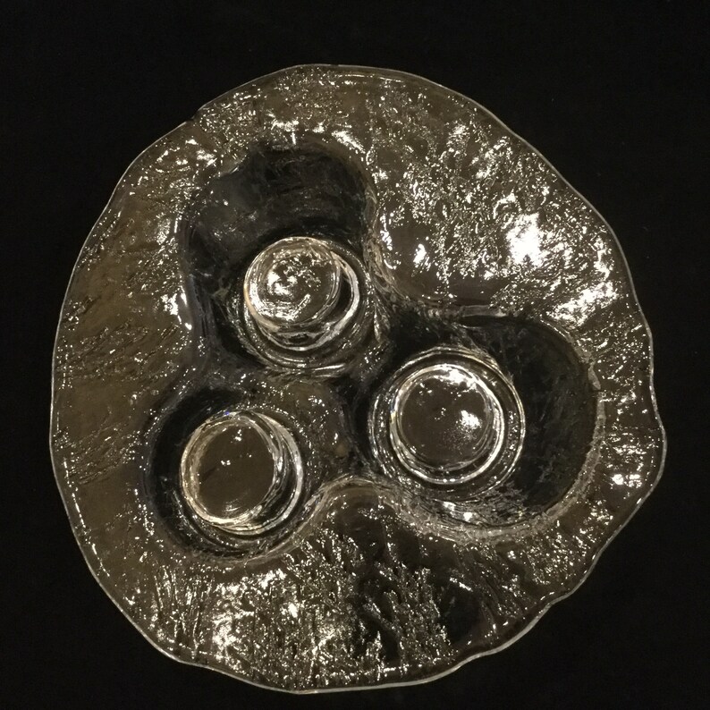 May include: A clear glass dish with three indented circular areas for holding small items. The dish has a textured, frosted surface.