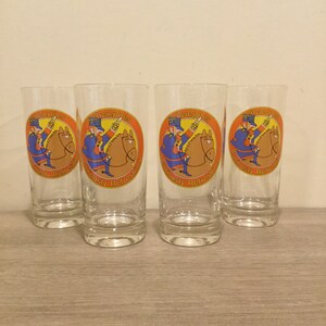 May include: Set of four clear glass tumblers with a red, orange, and blue Schweppes logo featuring a cartoon soldier riding a horse. The logo reads "Schweppes Curiously Refreshing".